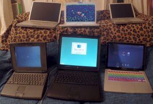 Six old laptops all open and lined up in two rows of three on a couch.