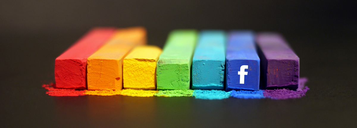 A group of seven rectangular box-shaped crayon sticks in different colors (from left to right: red, orange, yellow, light green, sky blue, dark blue, and purple); a white lower case f (the Facebook logo) appears on the front of the penultimate one (the one in dark blue). 